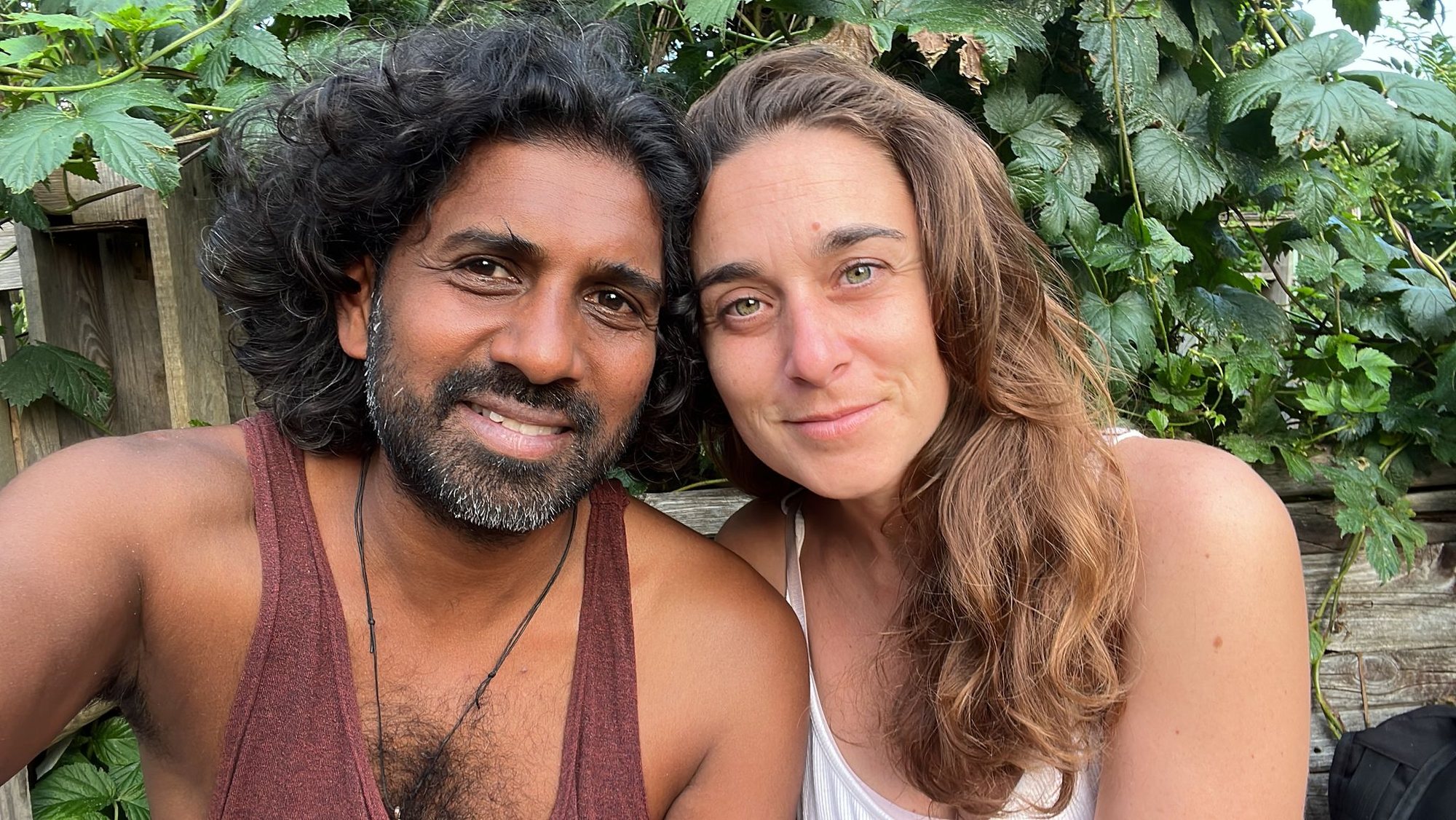 Ahilan and Fanny sitting together outdoors in front of a green, leafy wall