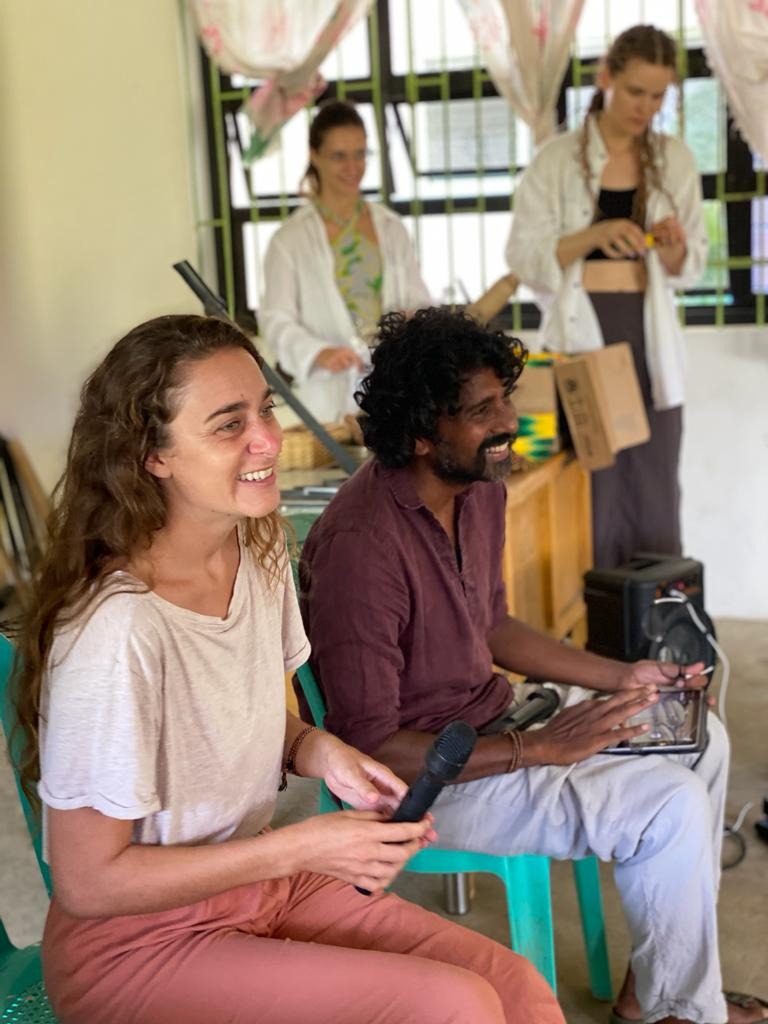 Fanny und Ahilan sitzen nebeneinander und lächeln, mit einem Mikrofon und einem Soundcontroller, hinter ihnen stehen zwei Personen