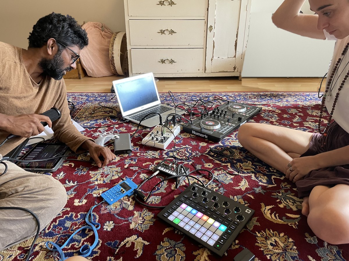 Ahilan und Fanny sitzen auf einem gemusterten Teppich, dazwischen Laptop, Mixer, DJ-Controller und Pad-Controller