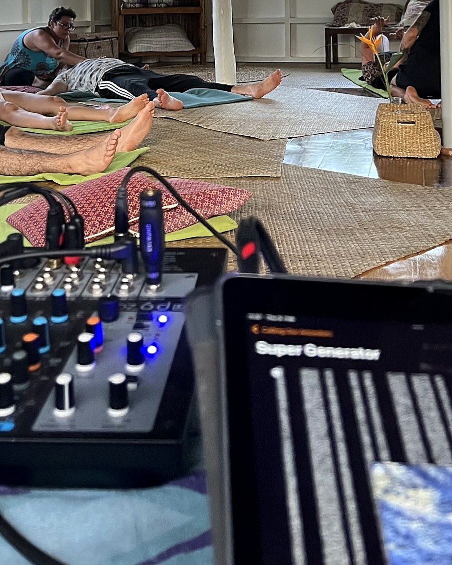 Ein Mischpult und ein Tablet bei einer Live-Playlisting-Session, im Hintergrund ruhen Teilnehmende auf Matten