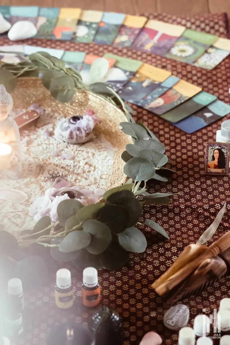 Ein für eine Session gedeckter Tisch: im Bogen ausgelegte Orakelkarten, ein geflochtener Korb mit Blumen und Kristallen sowie Eukalyptusblätter auf einem gemusterten Tuch